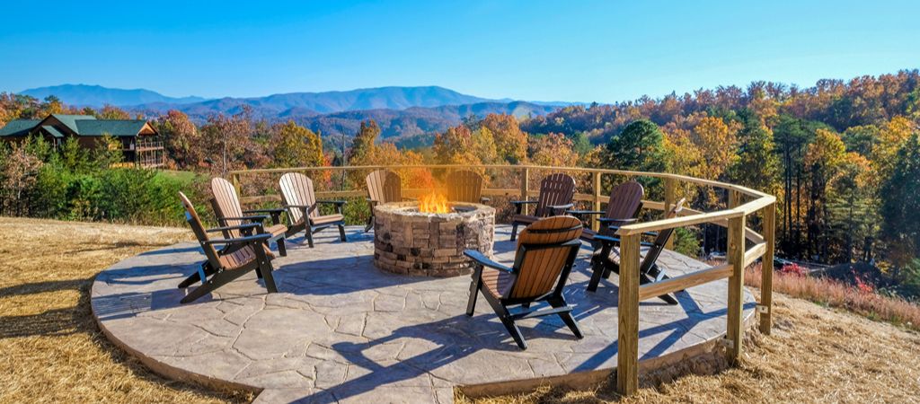 A large firepit with surrounding chairs invites cabin guests to unwind in front of a gorgeous Smoky Mountain view.